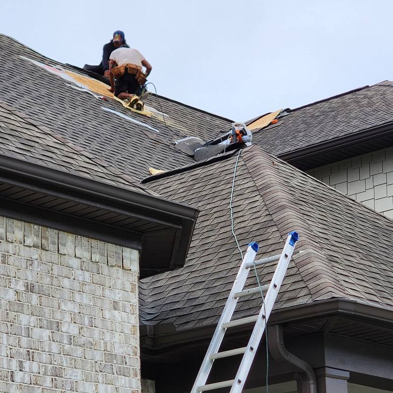 Roofing crew repairing roof decking on a brick home