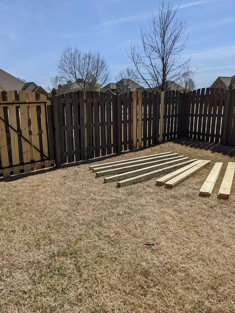 Wood privacy fence with lumber staged for repair